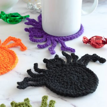Halloween crochet spider coasters on a table with a mug.
