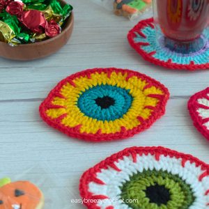 A yellow Halloween crochet eyeball coaster.