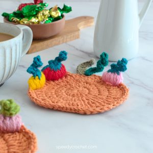 A pumpkin coaster on a table next to a mug.