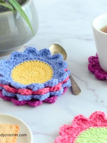 A set of crochet flower coasters in pink, blue and purple.