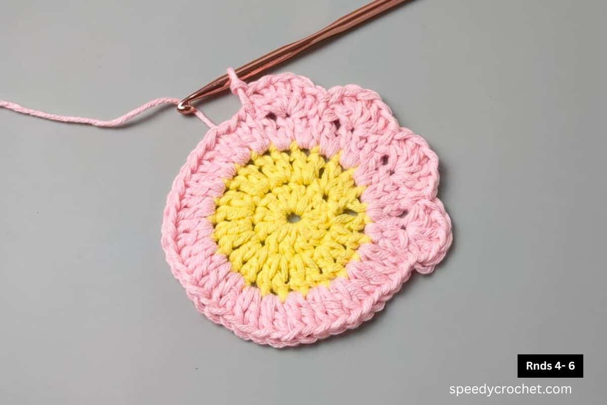 Yellow, pink crochet circle with a scallop edge.