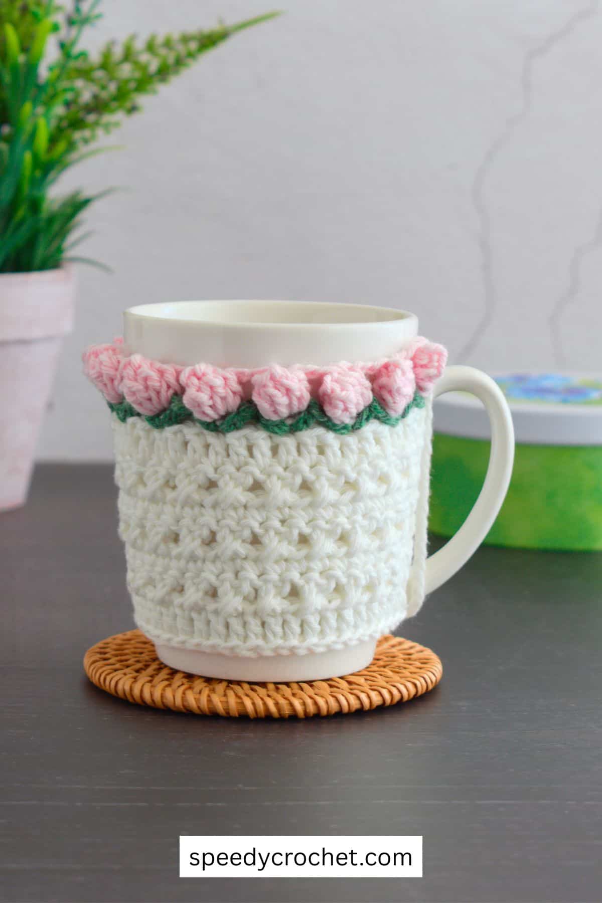 A pink and white crochet mug cozy.