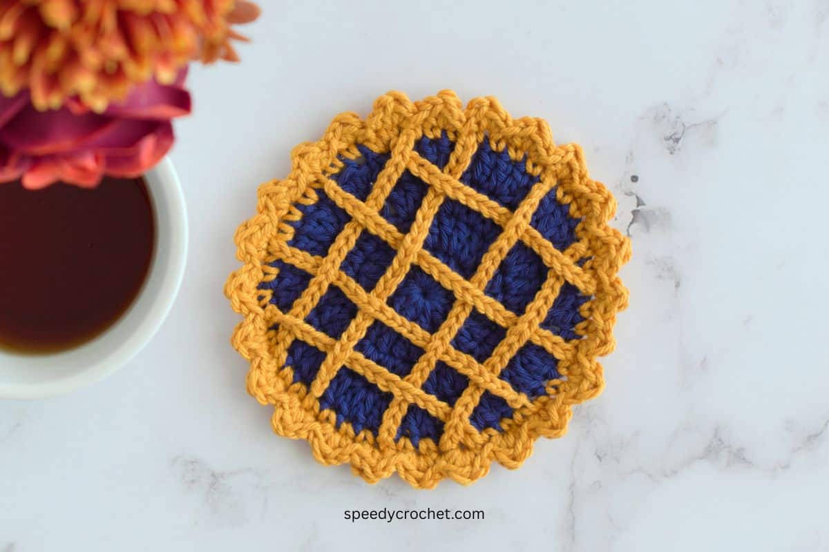 Pie crochet coaster made with blue and gold yarn.