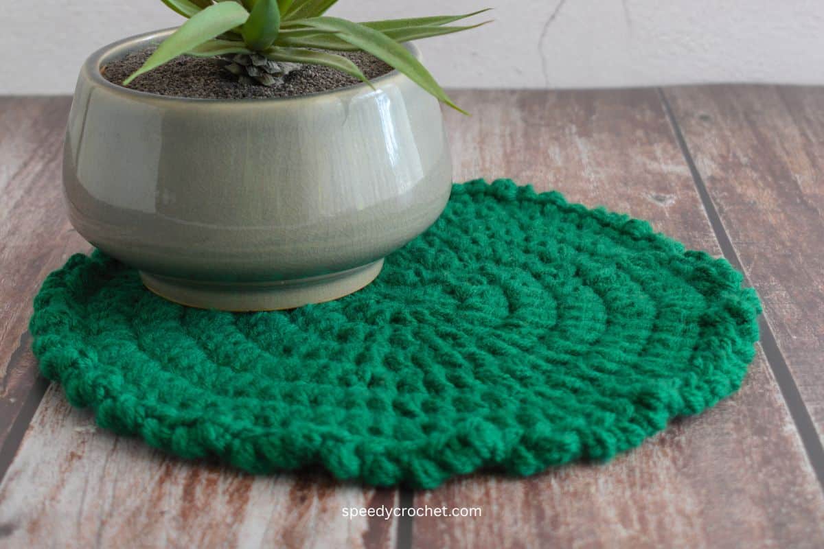 A crochet table mat on a wooden surface.